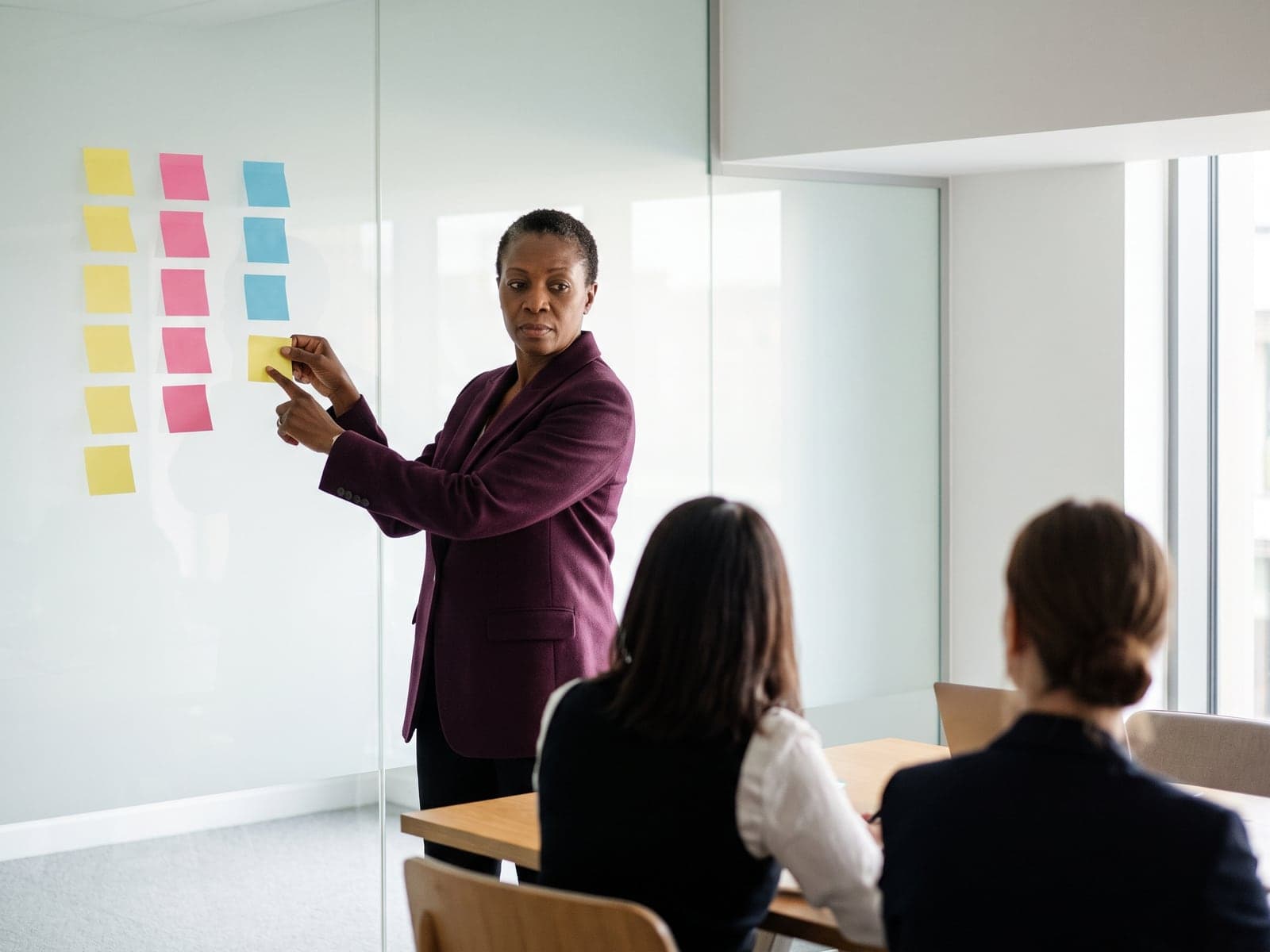 A consultant places a sticky note on a glass wall during an AI strategy workshop.