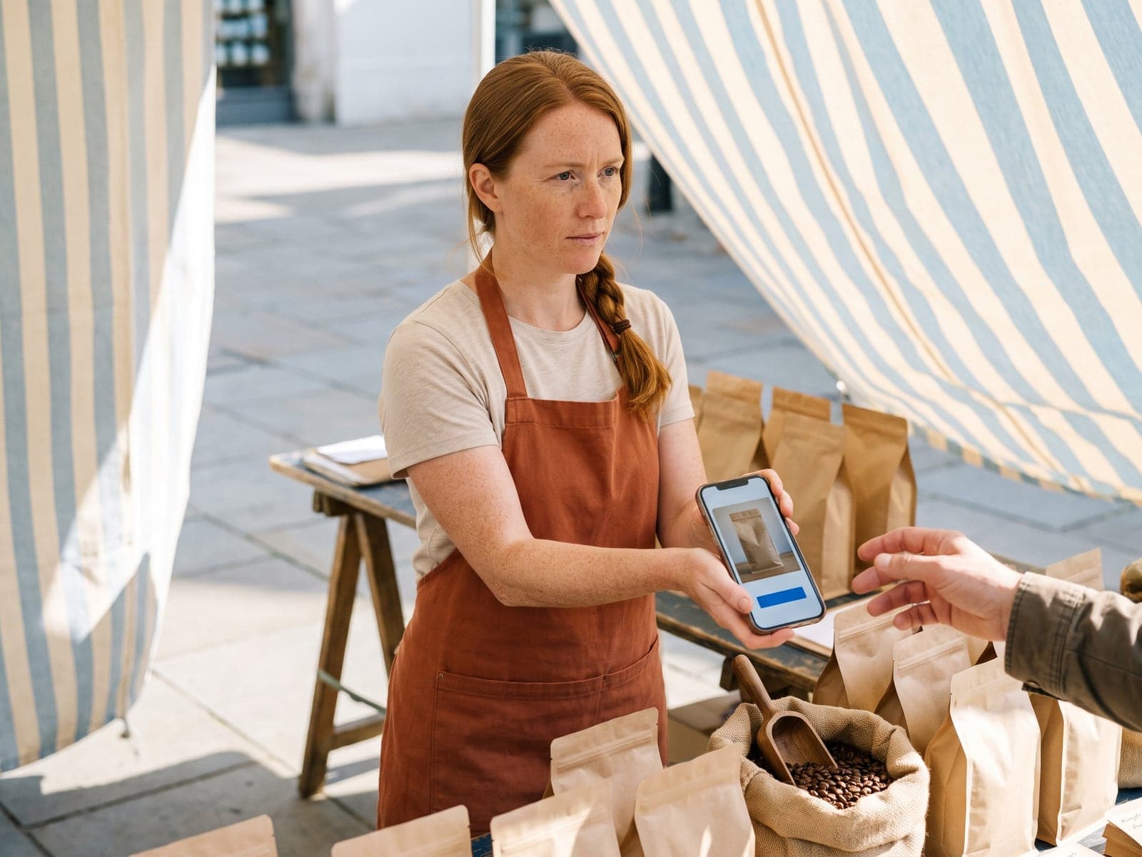A coffee roaster shows a customer a one page order screen on her phone at a market stall.