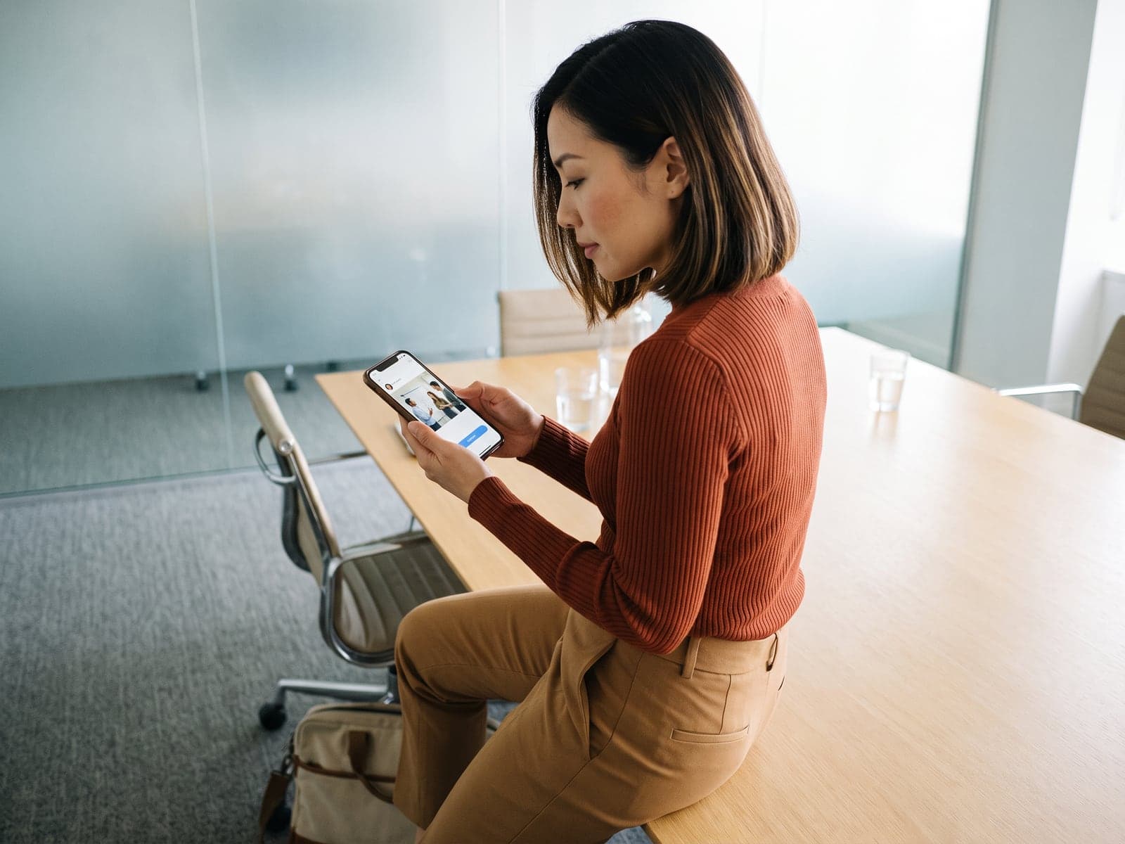 A founder sits on a boardroom table after a meeting and drafts a post with a team photo on her phone.