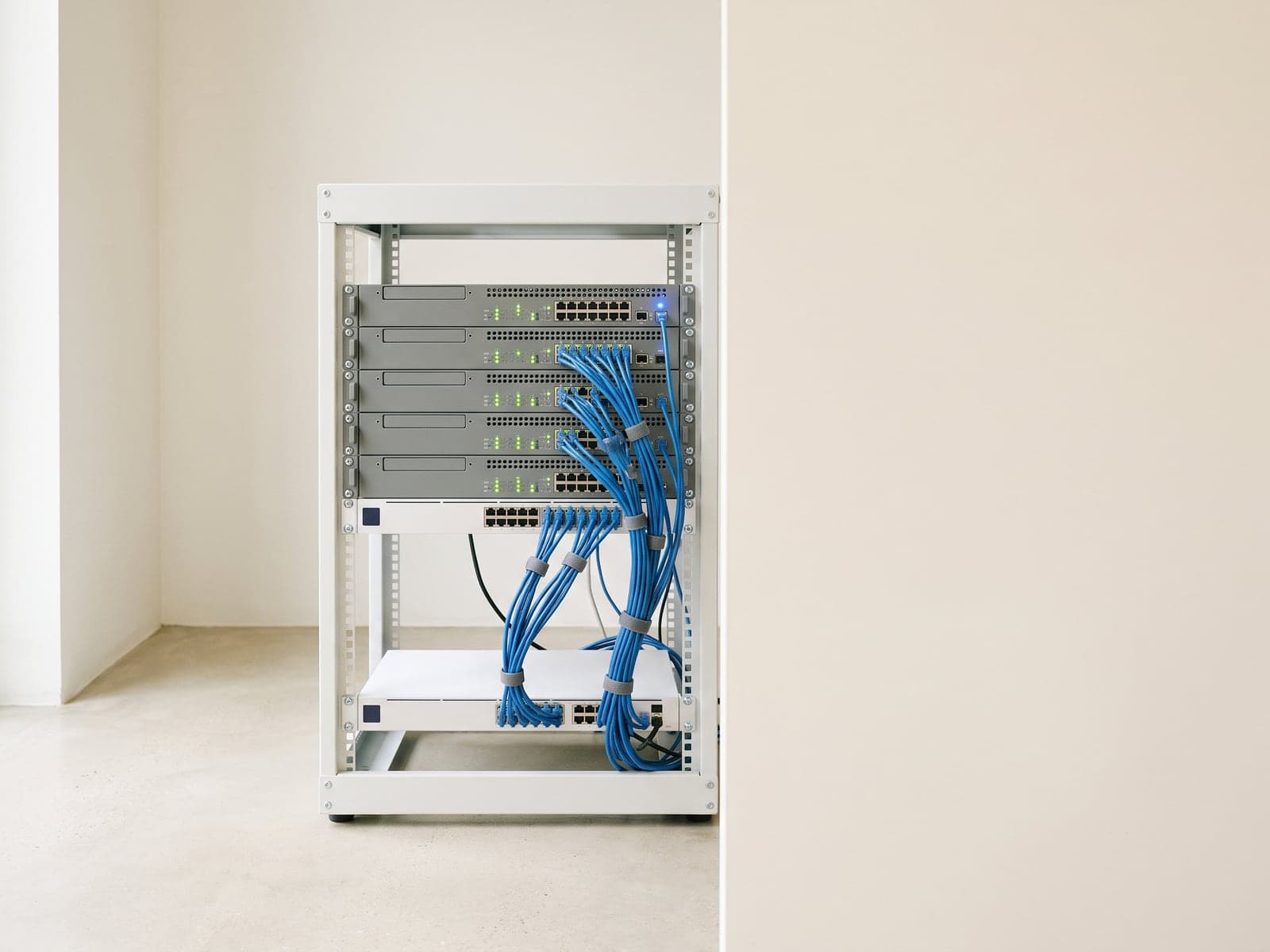 A compact open rack of servers with green status lights and bundled blue cables stands in a bright office corner.
