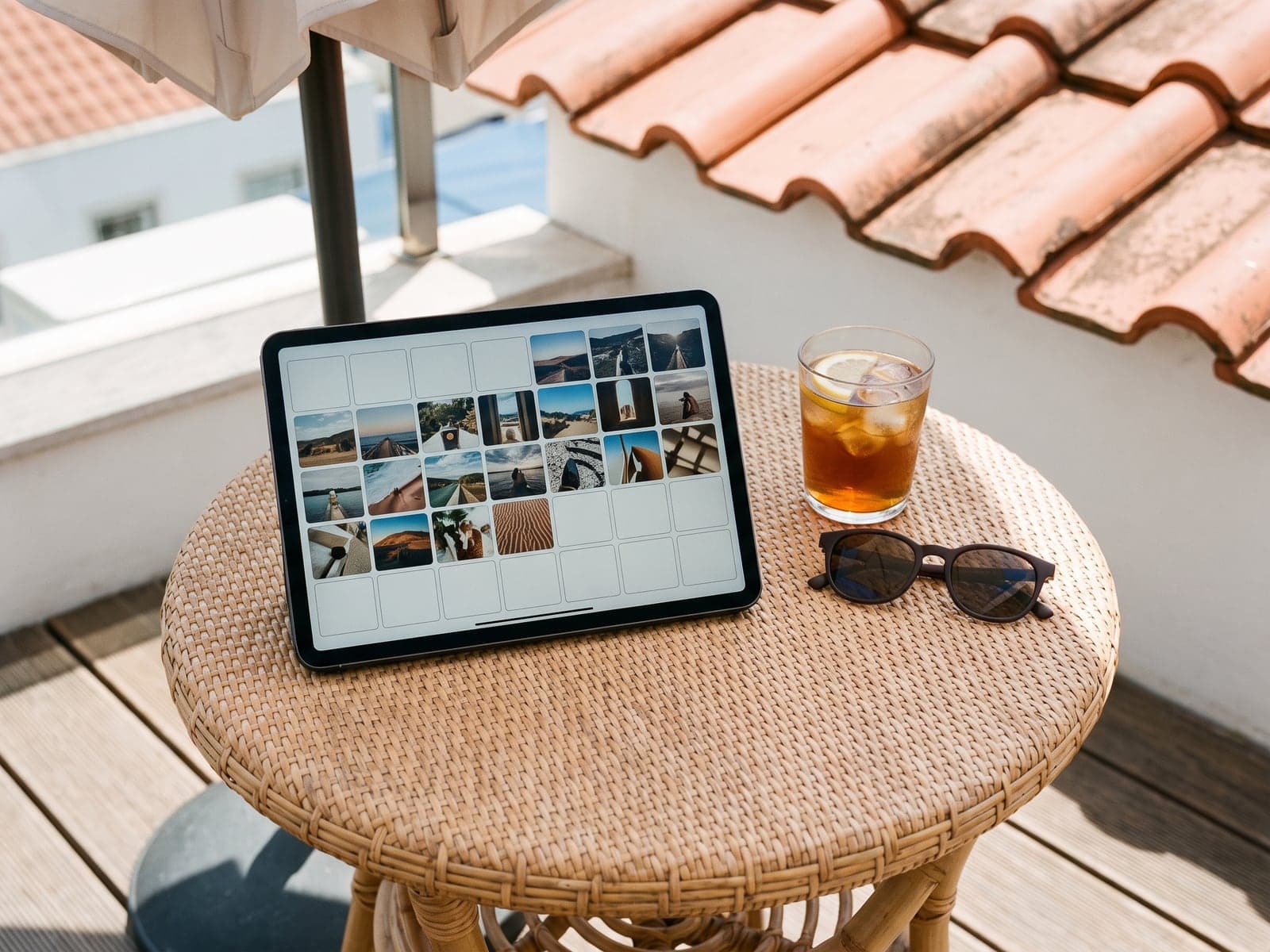 A tablet on a rooftop terrace table shows a month of scheduled social posts as photo tiles.
